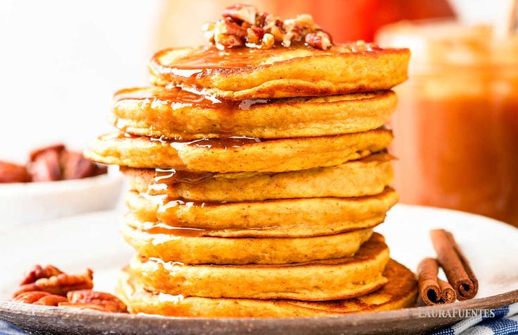 a stack of pancakes sitting on top of a white plate covered in syrup and pecans