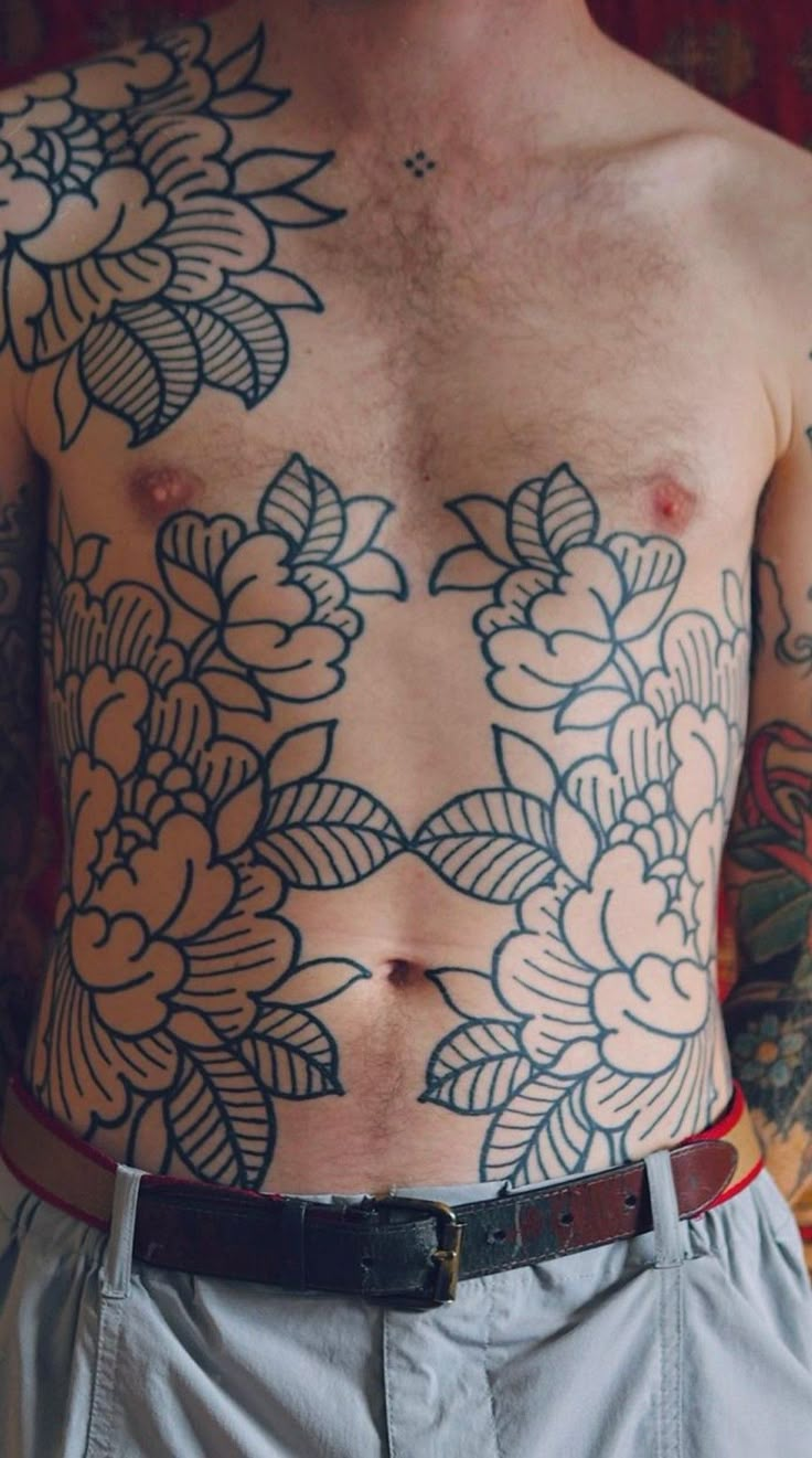 a man with tattoos on his chest standing in front of a wall