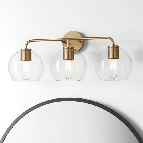 three light bathroom fixture with clear glass globes and brass finish on the vanity mirror