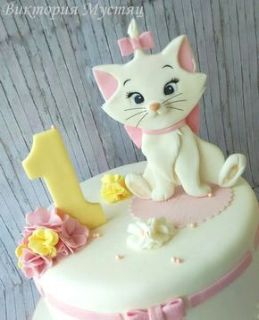 a white cake with pink and yellow frosting on the top has a cat sitting on it