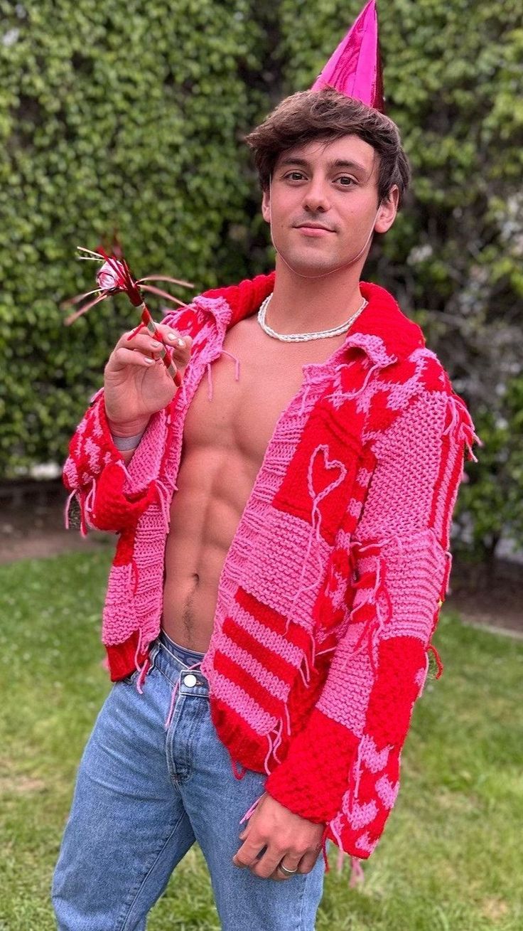 a shirtless man wearing a pink hat and holding a flower