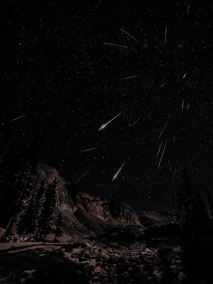 the night sky is filled with stars and shooting comets in the distance over mountains