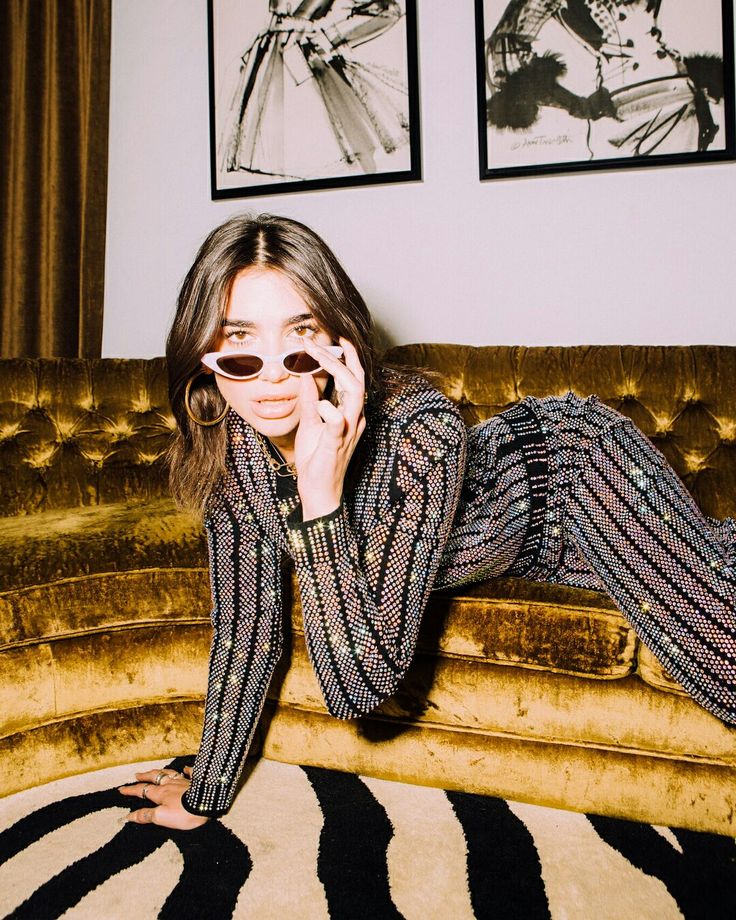 a woman laying on top of a couch talking on a cell phone while wearing sunglasses