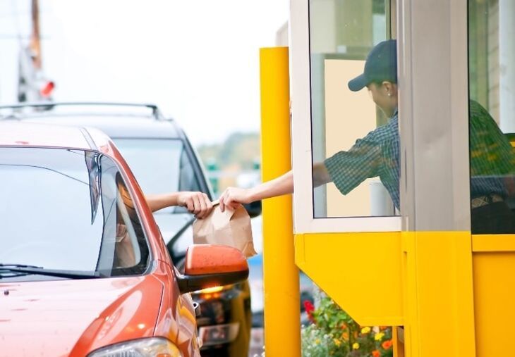 a man in a green shirt is opening the door of a red car and holding a brown paper bag