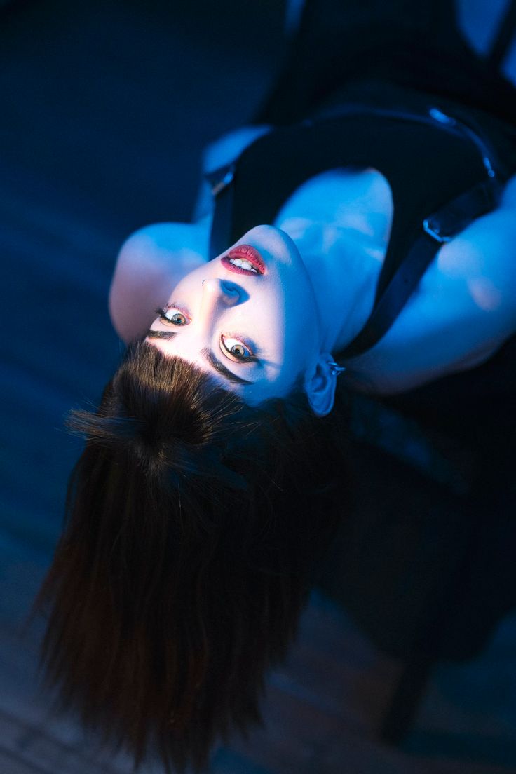 a woman with black hair and white makeup is upside down on the floor while holding her head up