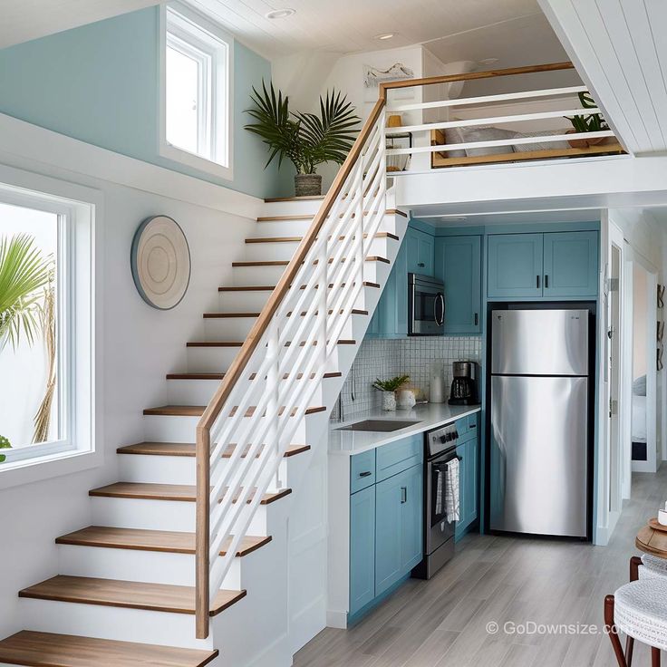 a kitchen with blue cabinets and stairs leading up to the upper floor, next to a stainless steel refrigerator