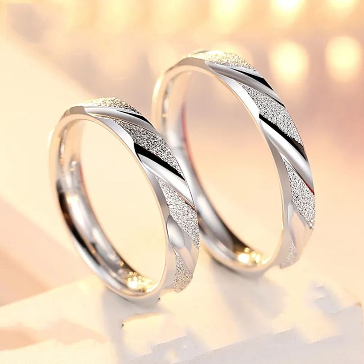 two wedding rings sitting on top of a white table next to each other with diamonds in them