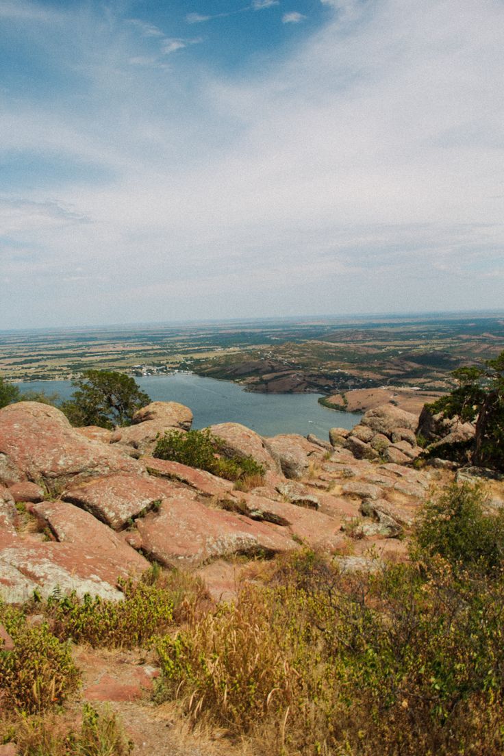 there is a bench on the top of a hill overlooking some water and land in the distance