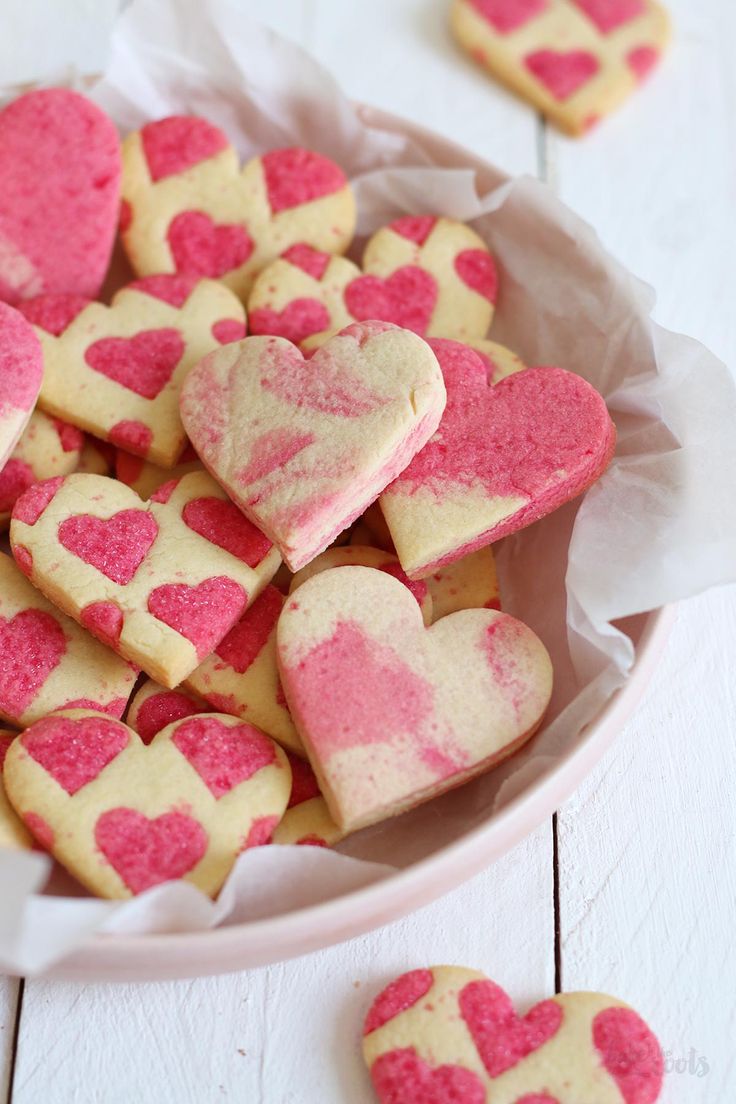 pink and white heart shaped sugar cookies in a bowl on a white table with other hearts