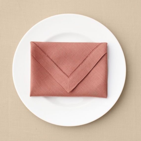 a white plate topped with an envelope on top of a beige tablecloth covered in pink linen