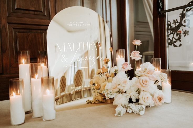 flowers and candles are sitting on the table next to a mirror with a wedding sign