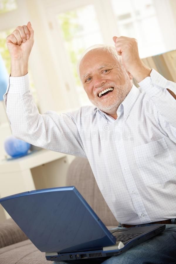 an old man sitting on a couch with his laptop in front of him and celebrating