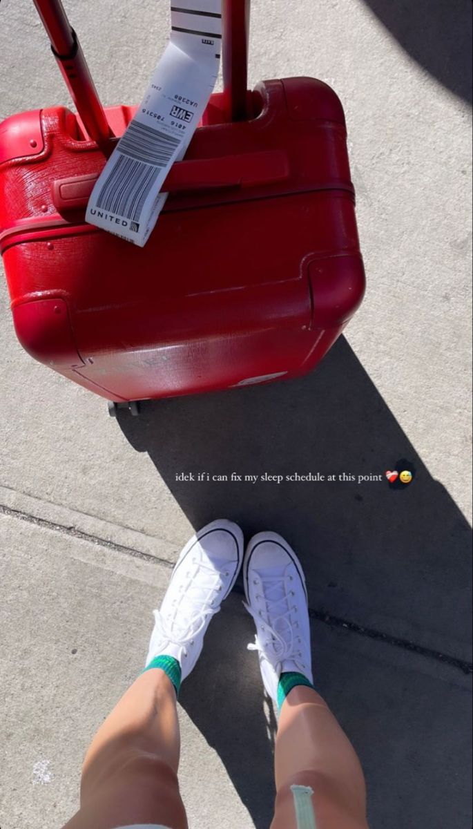 a person standing next to a red piece of luggage with a tag on it's handle