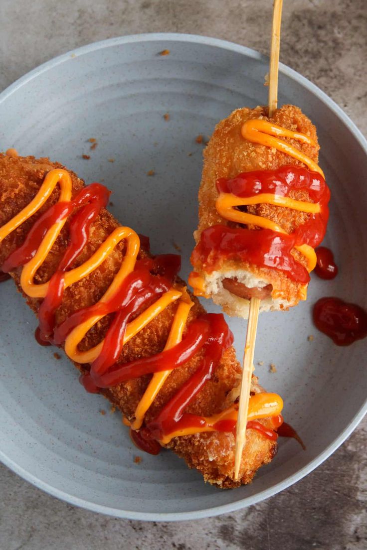 two hotdogs with ketchup and mustard are on a stick in a blue bowl