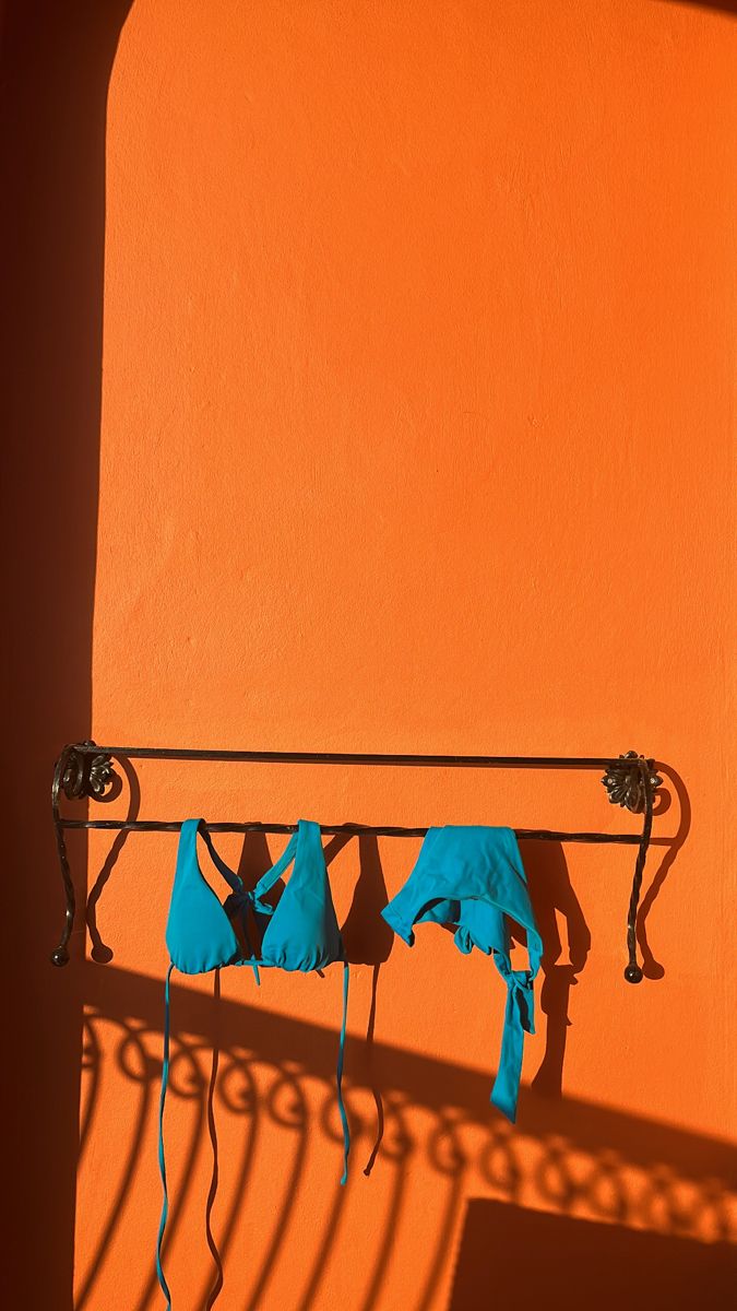 three blue towels are hanging on a metal rack in front of an orange stucco wall