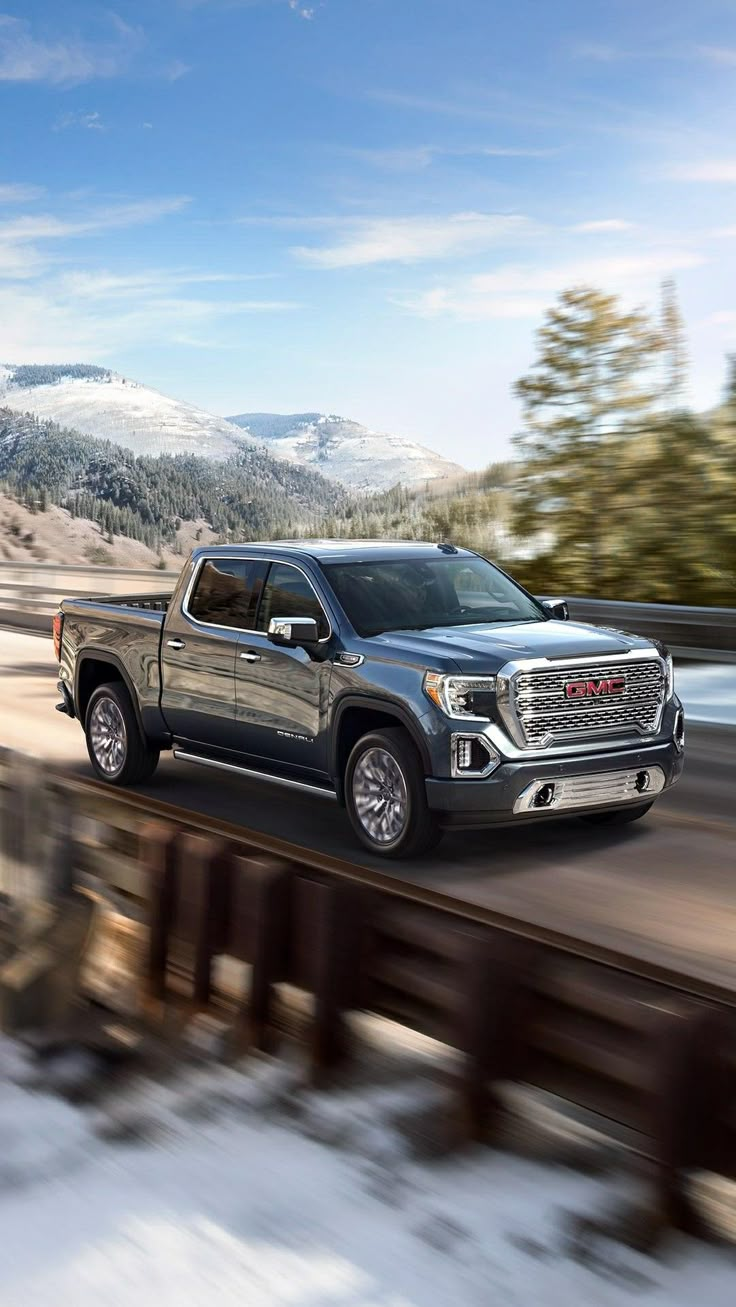 a gray truck driving down a road next to snow covered trees and mountains in the background