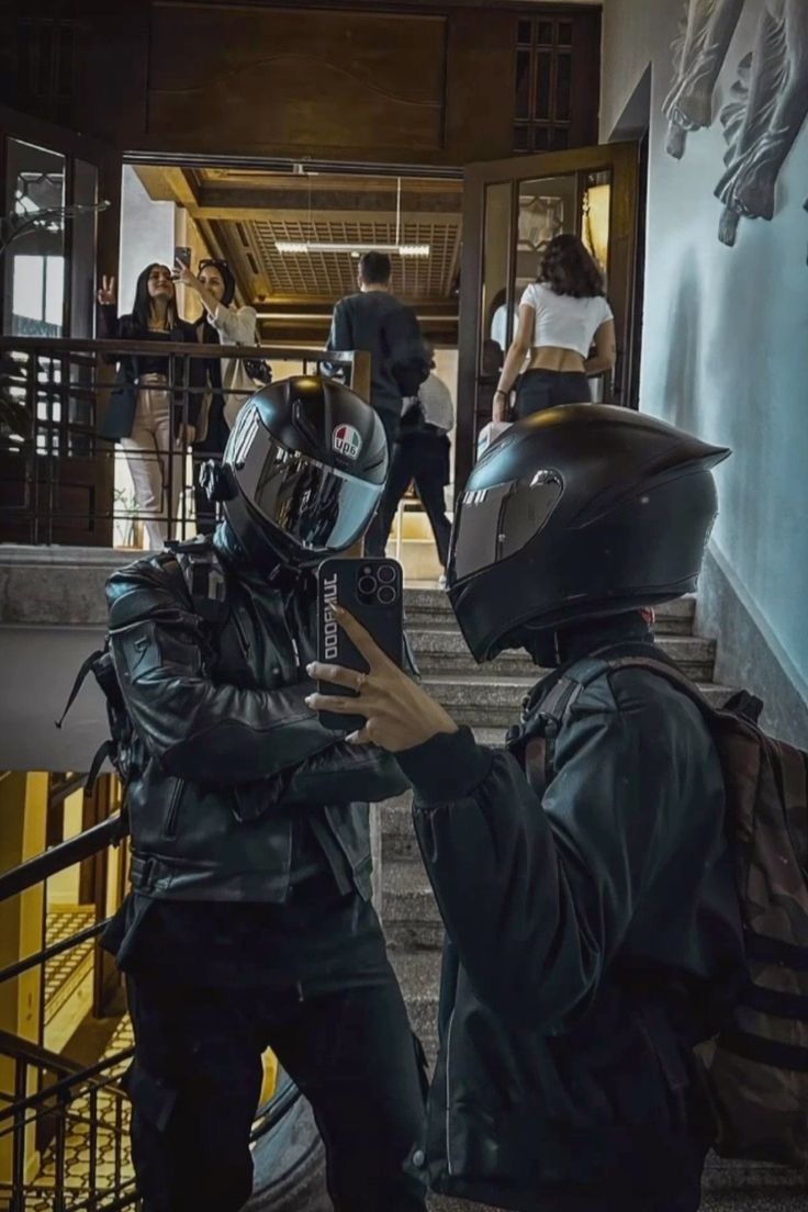 two people in helmets are standing on the stairs and one person is taking pictures with his cell phone