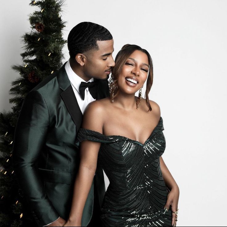 two people standing next to each other in front of a christmas tree