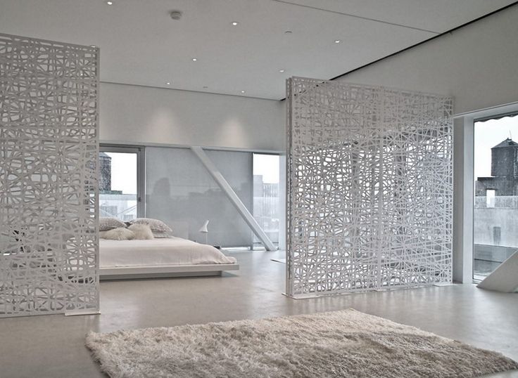 a bedroom with white walls and flooring next to a large glass door that opens onto a balcony