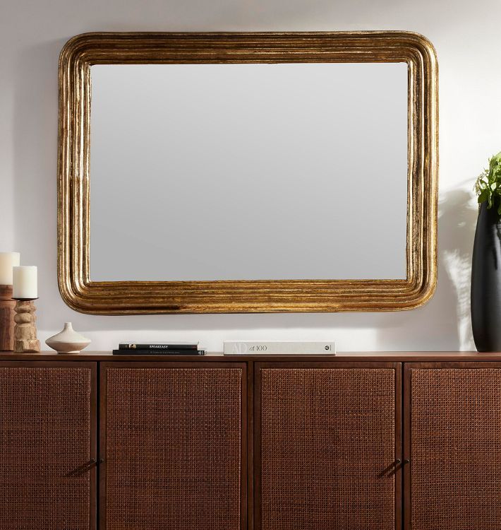 a large gold framed mirror sitting on top of a wooden dresser next to a vase