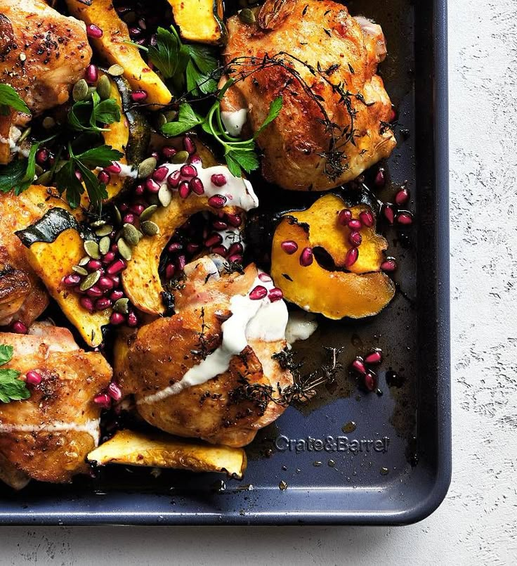 a tray filled with chicken, potatoes and pomegranates