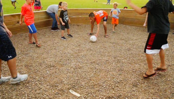 a group of children playing with a soccer ball in a circle on the ground at a park