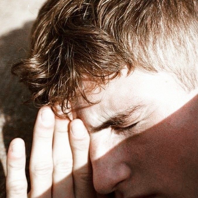 a close up of a person holding their hand to his face with the sun shining on them