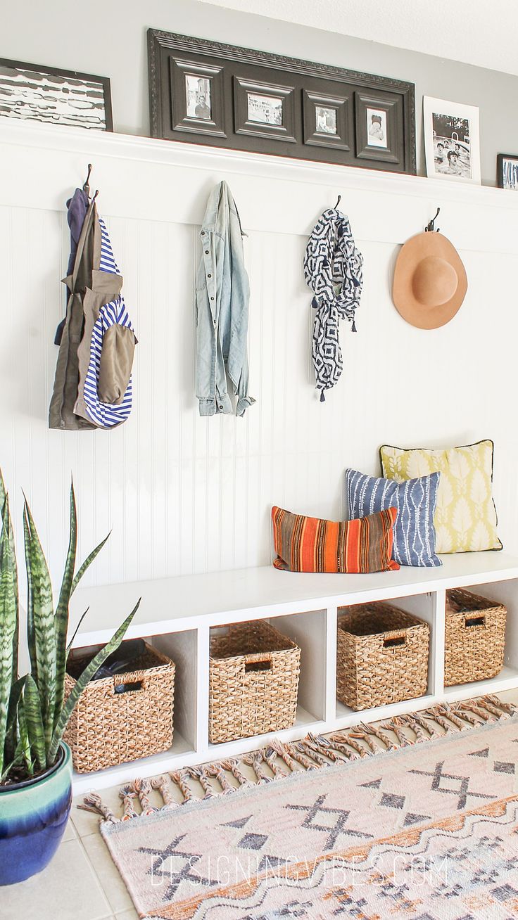 a white bench sitting next to a wall filled with lots of baskets and hanging items