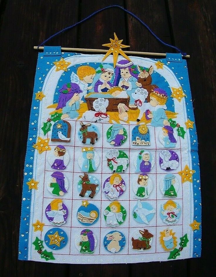 a cross stitch nativity calendar hanging on a wooden wall with blue string and pegs