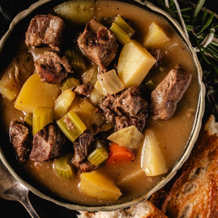 a bowl filled with meat and vegetables next to bread