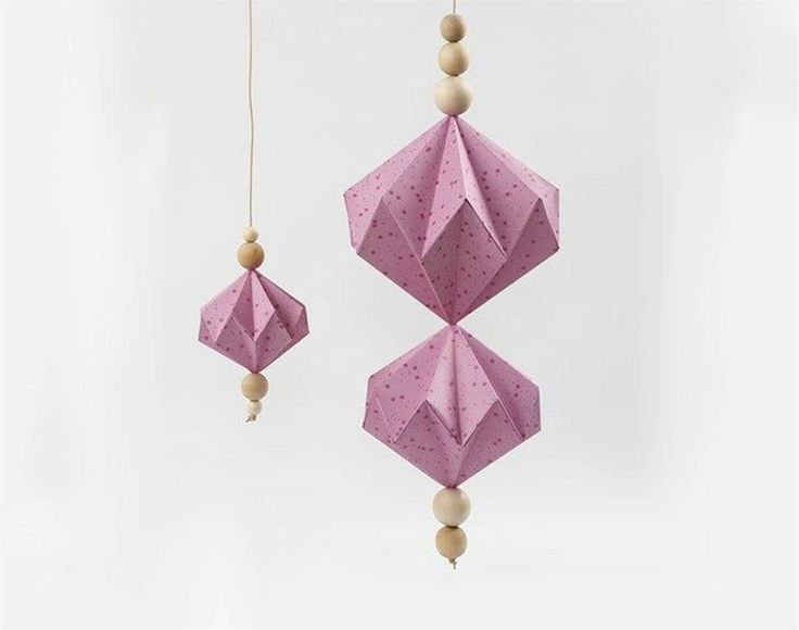 two pink origami ornaments hanging from strings on a white background with polka dots