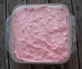 a pink cake in a plastic container on a wooden table