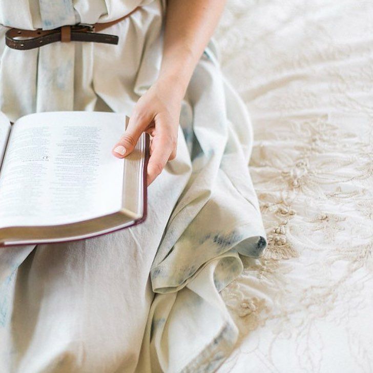 a person sitting on a bed with a book in their lap and one hand holding an open book