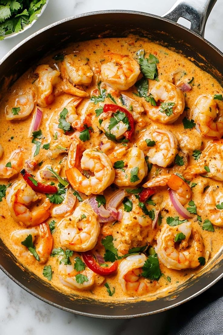 a skillet filled with shrimp and vegetables on top of a white marble countertop