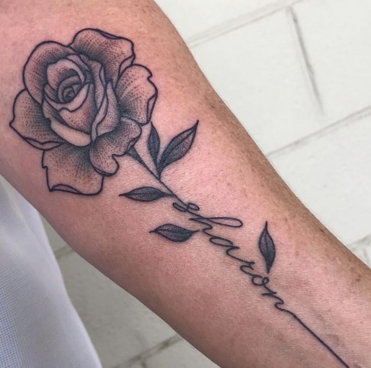 a black and white rose tattoo on the left arm with words written in cursive writing