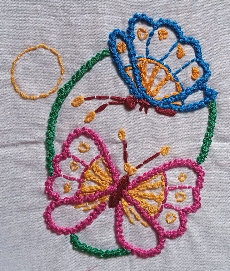 three colorful butterflies on a white cloth with yellow, blue and pink threadwork in the middle