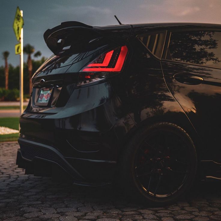 the back end of a black car parked on a cobblestone road at dusk