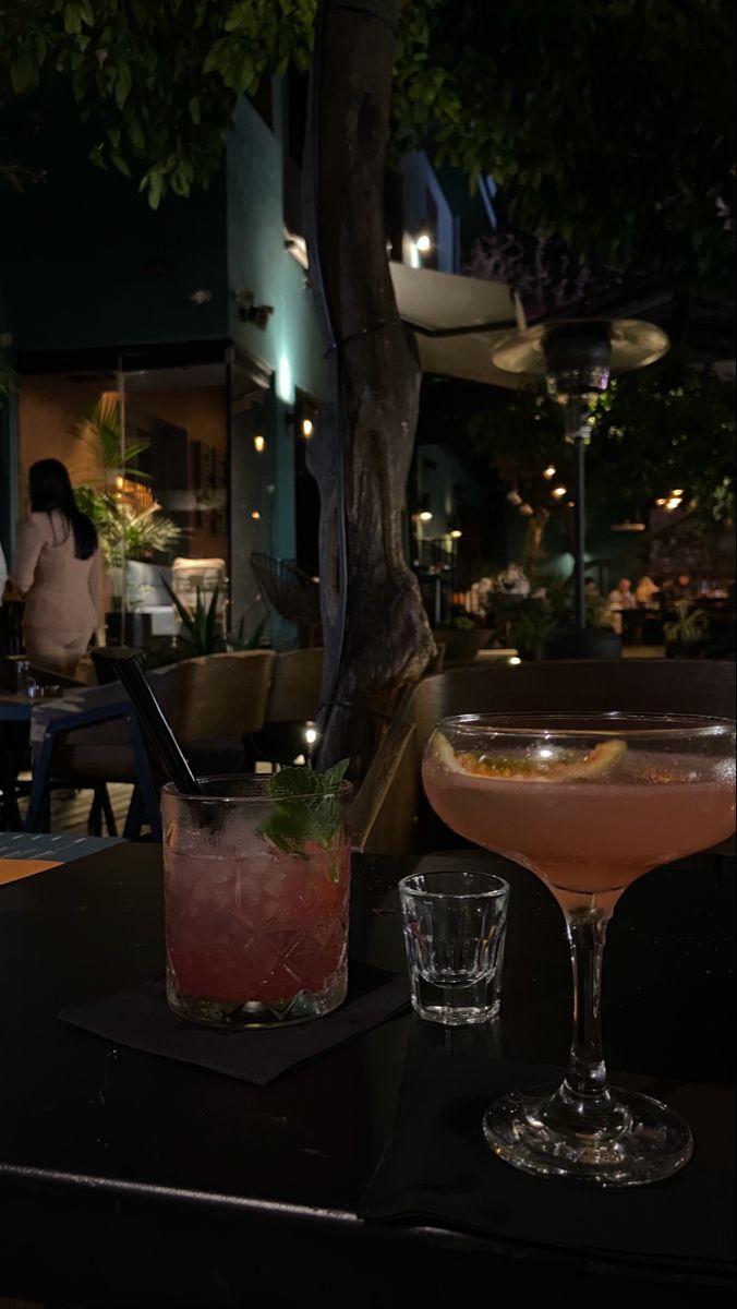 two cocktails sitting on top of a table next to each other in front of a tree