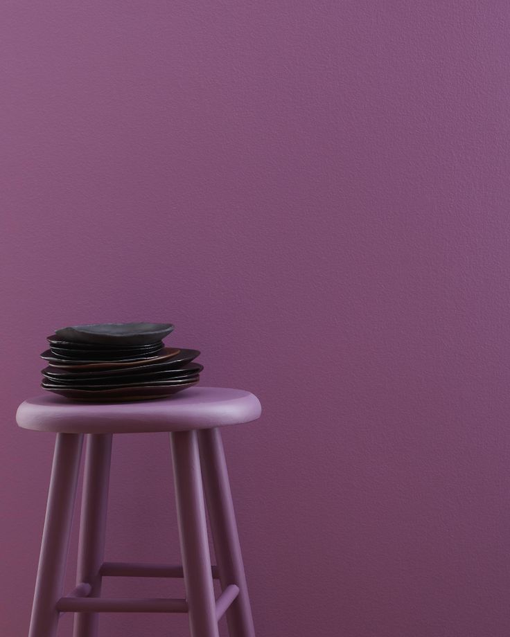 a stack of black plates sitting on top of a stool next to a purple wall