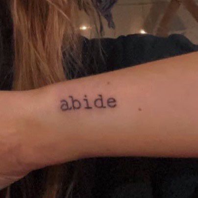 a woman's arm with the word abide tattooed on it