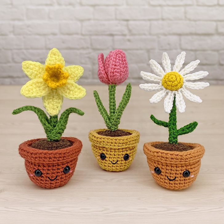 three crocheted potted plants with flowers in them, one has a smiley face