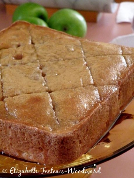 a piece of bread sitting on top of a cutting board next to some green apples