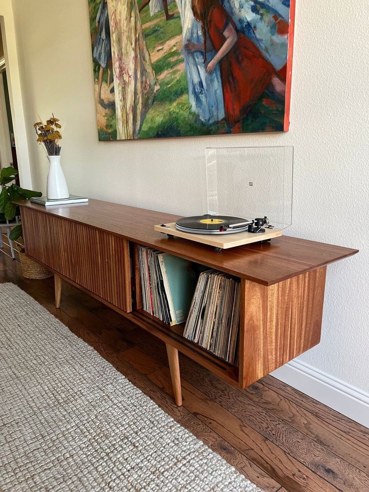 a record player sitting on top of a wooden cabinet next to a painting and rug