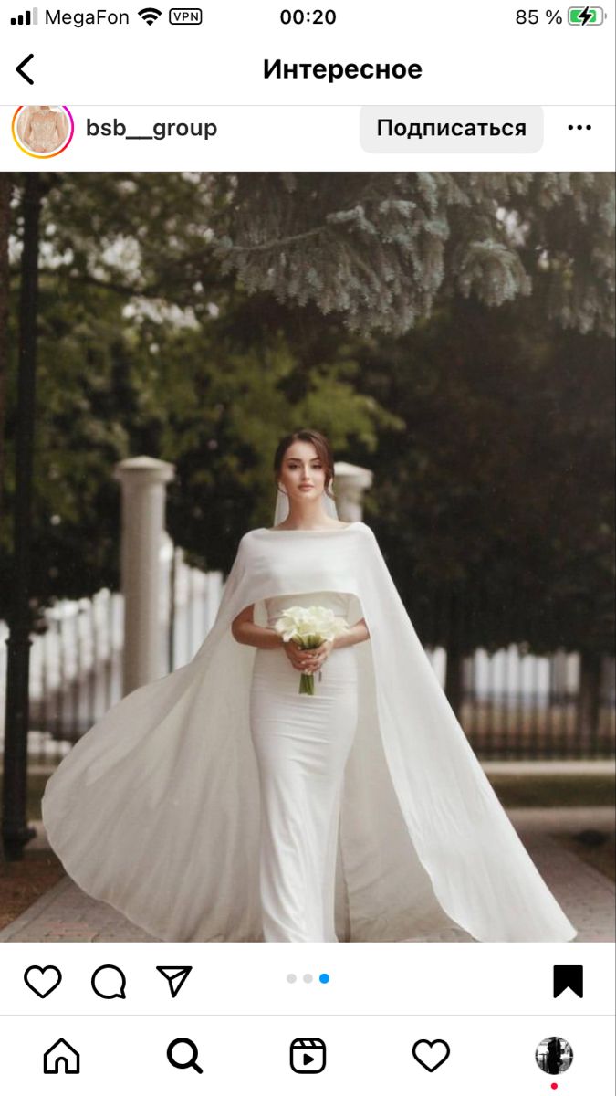 a woman in a white wedding gown holding a bouquet and wearing a long cape over her shoulders