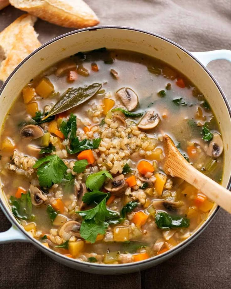 a pot full of soup with mushrooms, carrots and spinach on the side