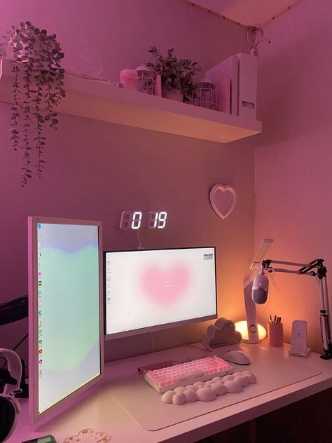 a desk with two computer monitors and a keyboard on it in front of a pink wall