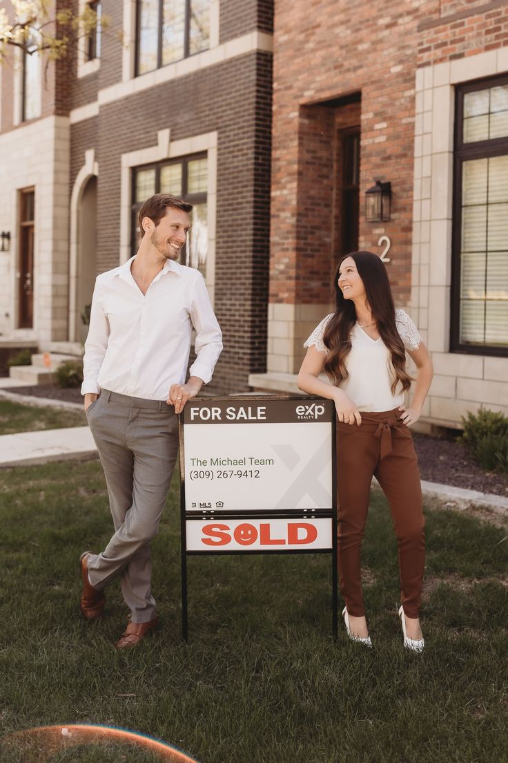 a man and woman standing next to a sold sign