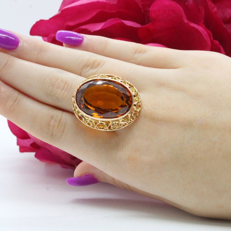 "This is a gorgeous golden Vintage Synthetic Orange Sapphire Gemstone Statement Ring, set in 14K Yellow Gold. The Ring showcases a center Synthetic Orange Sapphire, measuring 24 x 17 mm, totaling 56.58 CTW, set in an ornately designed 14K Yellow Gold Bezel Setting. The Ring is a Size 8.25 (Resizable). This stunning piece of Fine Vintage Gemstone Jewelry is being offered here for an unbeatable WHOLESALE price! A rare Vintage find! A true Golden Treasure! Metal: 14K Yellow Gold Hallmark: \" 14K\" Gold Oval Ring With Large Stone, Gold Jewelry With Large Round Stone, Gold Rings With Large Stone For Anniversary, Exquisite Gold Topaz Ring With Center Stone, Gold Topaz Ring With Large Stone As Gift, Antique Gold Topaz Ring With Center Stone, Luxury Gold Topaz Ring With Center Stone, Gold Topaz Ring With Center Stone, Luxury Style, Oval Gold Topaz Gemstone Ring