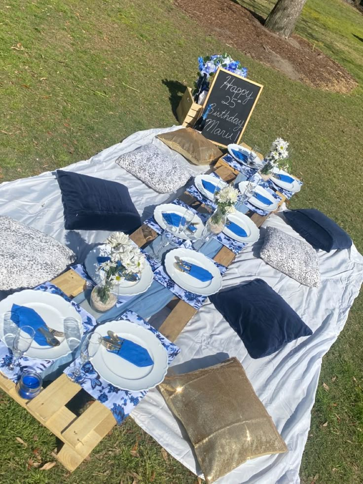 an outdoor table set up with blue and white plates, napkins and place settings