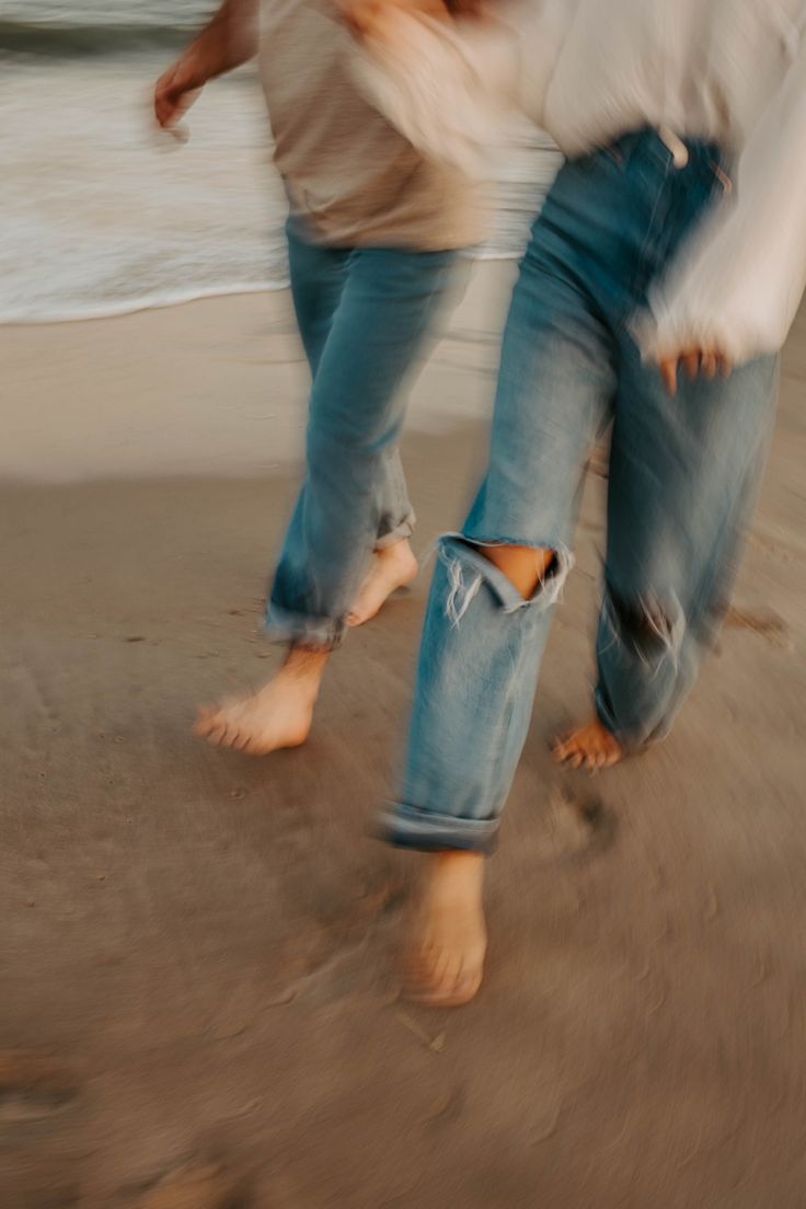 two people are walking on the beach with their feet in the sand and one person is wearing jeans